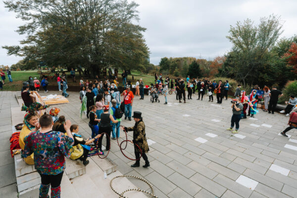 QUIET PARADE artists and attendees gather on large, open paved area at the end of the parade route in Fort Needham Park. The crowd is made up of cyclists, circus performers, people in costumes and wearable art and others in plain clothes.