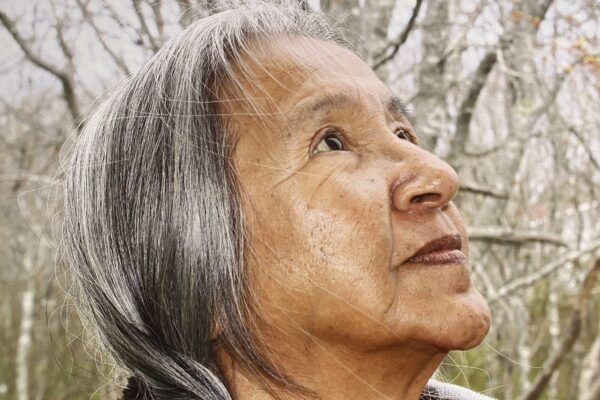 Image of a Mi'kmaq woman looking upwards to the right with snow-covered trees behind her.