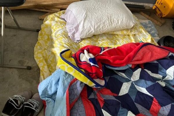 Image of a mattress covered with sheets and blankets on cement floor.