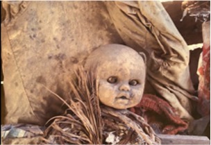 Image of a dusty, discarded doll among debris.